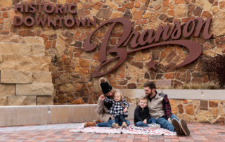family sitting in front of historic Branson sign on vacation
