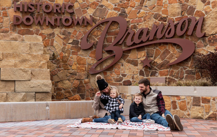 family sitting in front of historic Branson sign on vacation